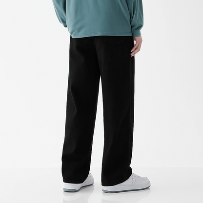 Man wearing black wide-leg relaxed fit denim jeans with teal long sleeve top and white sneakers, back view.