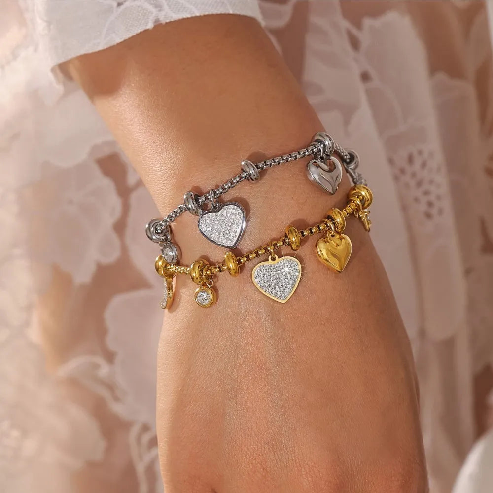 Woman wearing layered silver and gold heart charm bracelets with crystal pavé accents on delicate box chain links.