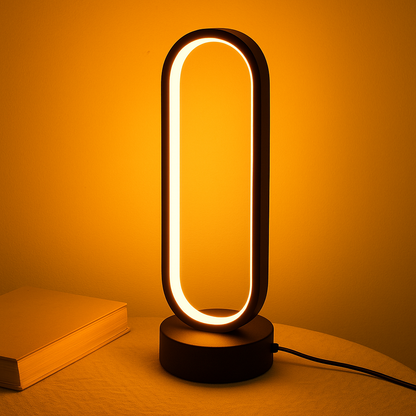 Modern LED desk lamp with warm orange glow and oval design on circular base with power cord