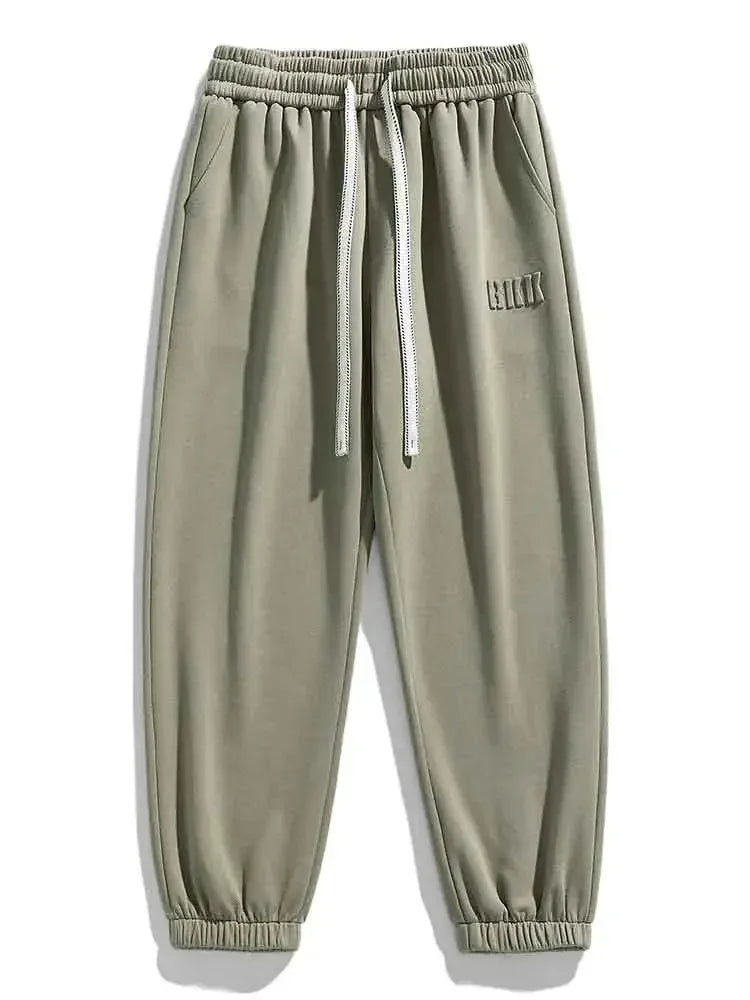 Sage green men's drawstring sweatpants with elastic waist, side pockets, ribbed cuffs, and small logo detail.