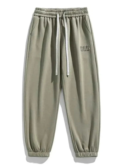 Sage green men's drawstring sweatpants with elastic waist, side pockets, ribbed cuffs, and small logo detail.