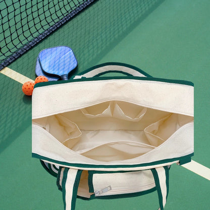 Viera canvas tote bag open on pickleball court showing interior pockets, green trim, with paddles and ball nearby.