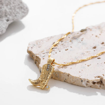 Gold western cowboy boot charm necklace with crystal accents on a twisted chain, displayed on stone surface.