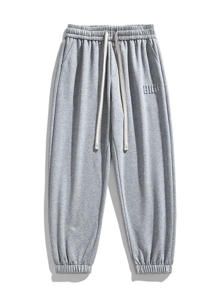 Gray men's tapered knit joggers with elastic waistband, drawstring, side pockets, and ribbed cuffs.