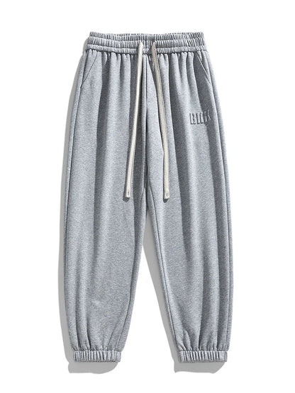 Gray men's tapered knit joggers with elastic waistband, drawstring, side pockets, and ribbed cuffs.