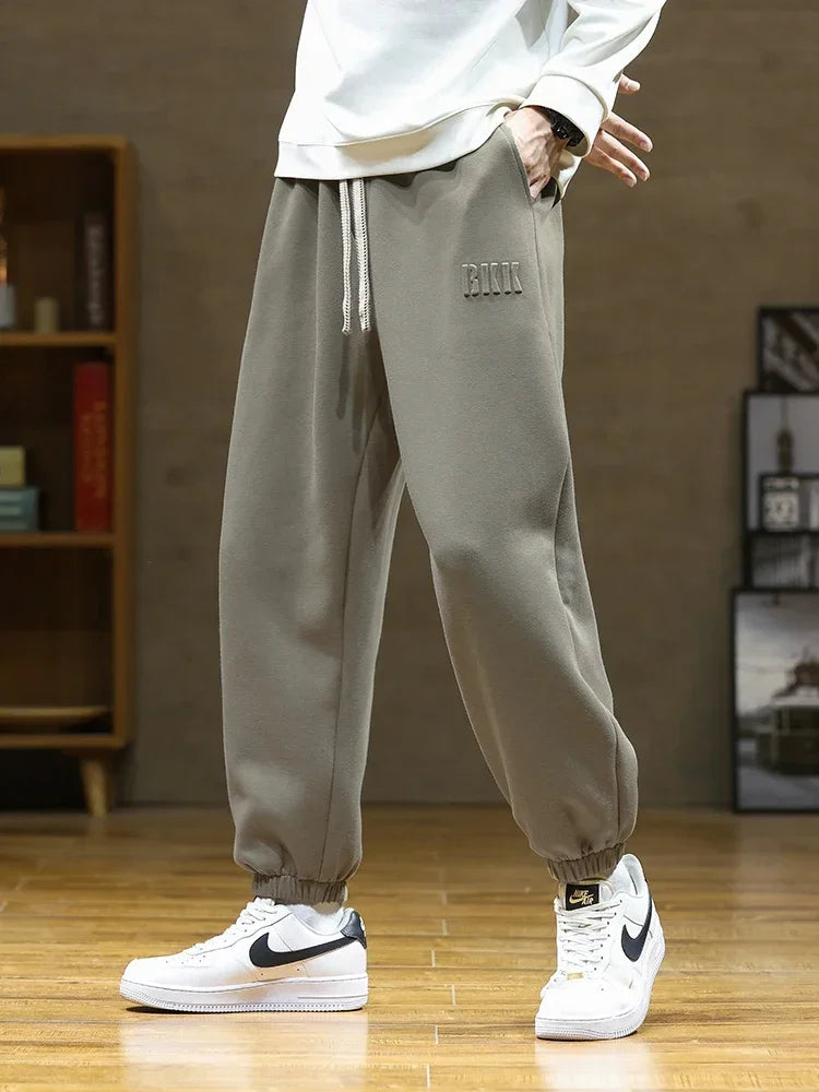Men's gray drawstring jogger sweatpants with elastic cuffs, worn with white Nike Air Force 1 sneakers and white sweatshirt.