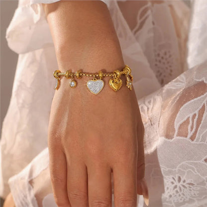 Gold chain charm bracelet with crystal heart, solid heart, moon, and star pendants worn on a woman's wrist