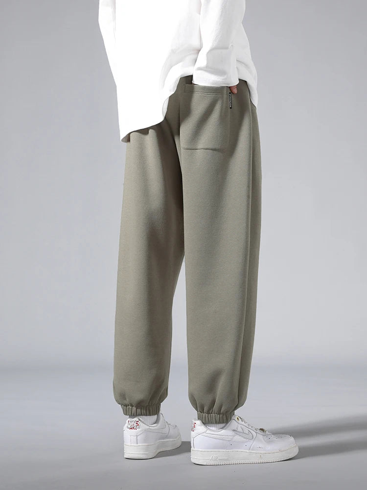 Men's sage green tapered knit joggers with elastic cuffs, paired with white Nike Air Force 1 sneakers and white top.
