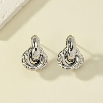 Silver interlocked knot hoop stud earrings with layered twisted rings, displayed on a cream surface