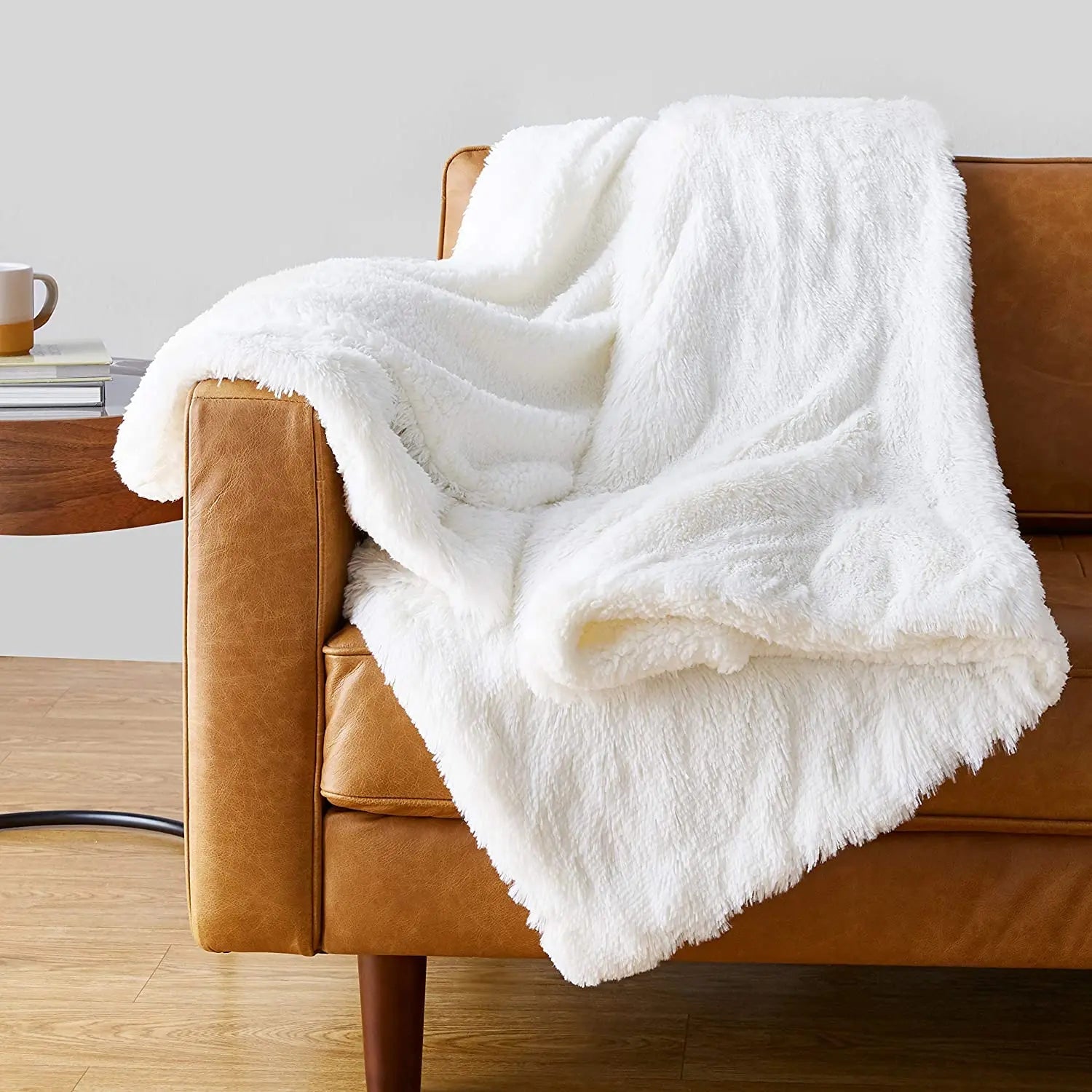Ivory faux fur plush throw blanket draped over a tan leather sofa in a cozy living room setting.