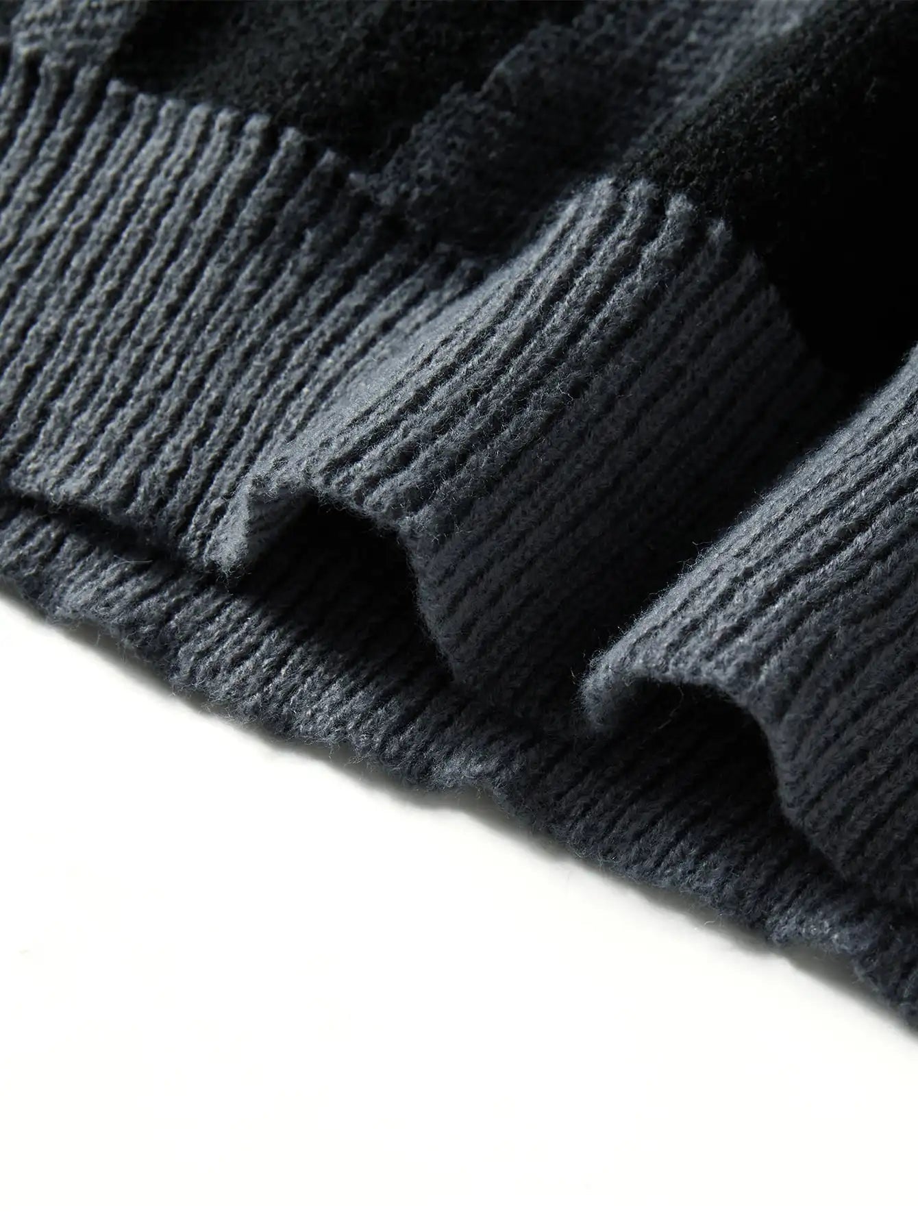 Close-up of dark grey wool knit oversized men's sweater showing ribbed hem detail and abstract texture pattern