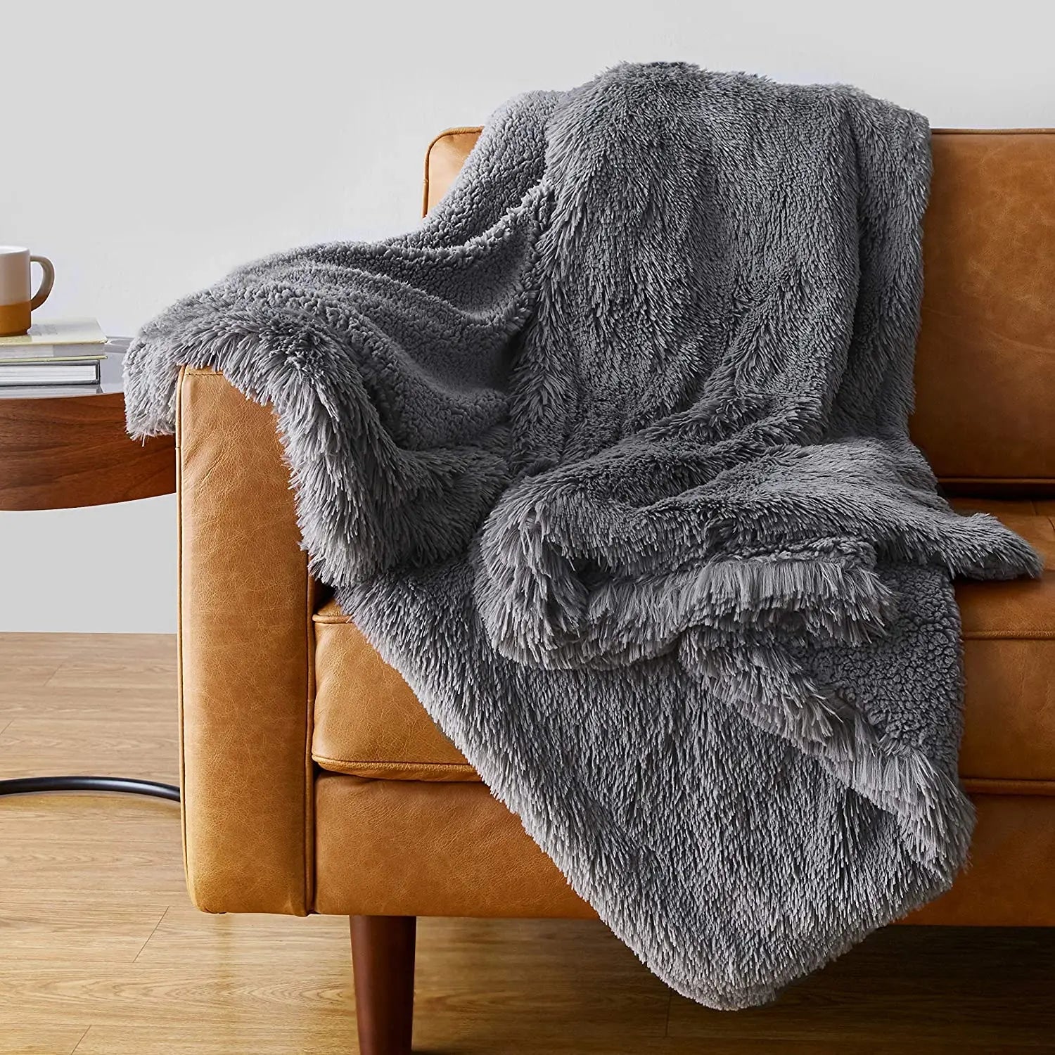 Gray faux fur plush throw blanket draped over a tan leather sofa in a modern living room setting.