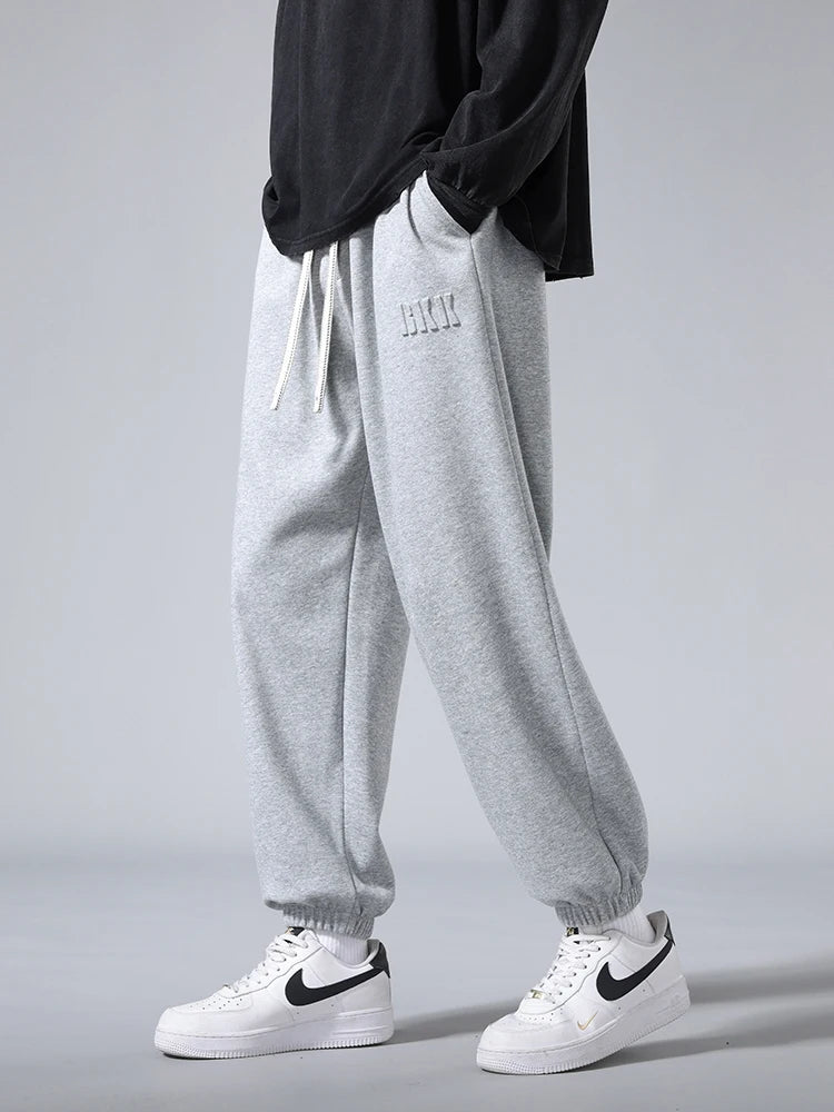 Men's gray tapered knit joggers with drawstring waist, ribbed cuffs, and subtle logo, styled with Nike Air Force 1 sneakers.
