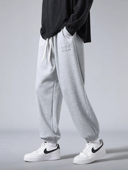 Men's gray tapered knit joggers with drawstring waist, ribbed cuffs, and subtle logo, styled with Nike Air Force 1 sneakers.