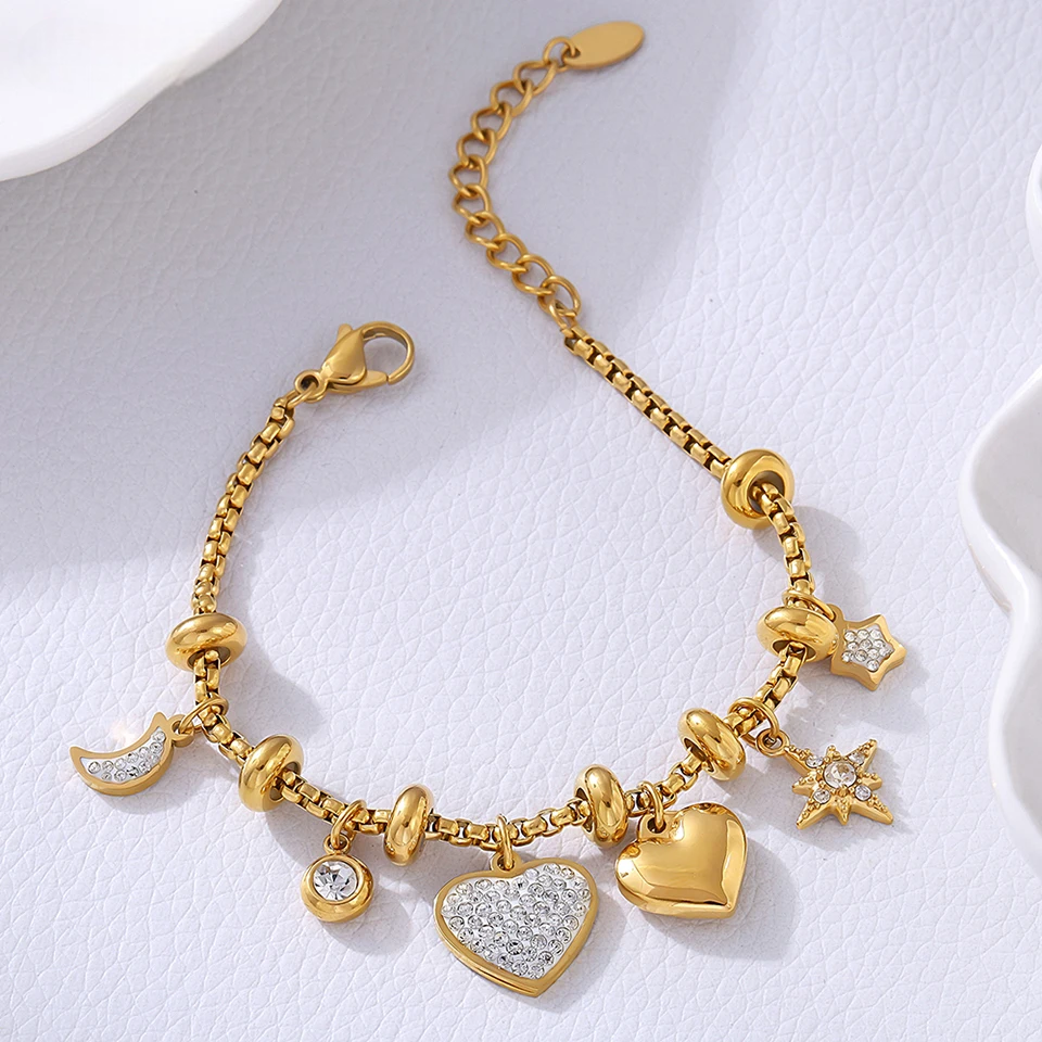 Gold heart charm bracelet with crystal moon star accents for women on white textured background