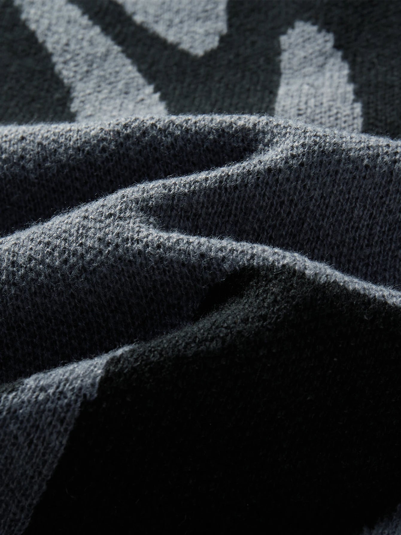 Close-up of dark charcoal wool knit fabric with grey abstract geometric pattern, showing soft textured weave detail