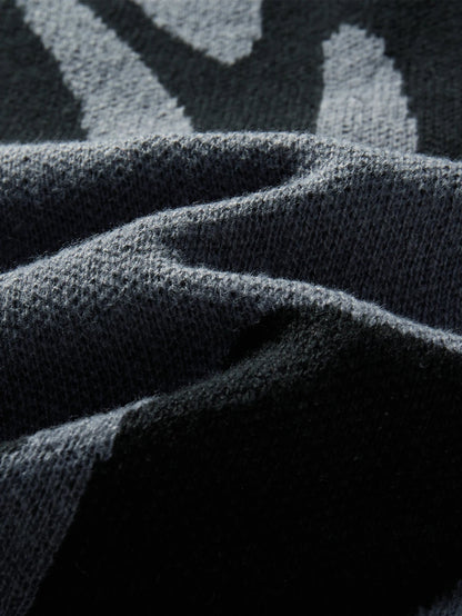 Close-up of dark charcoal wool knit fabric with grey abstract geometric pattern, showing soft textured weave detail