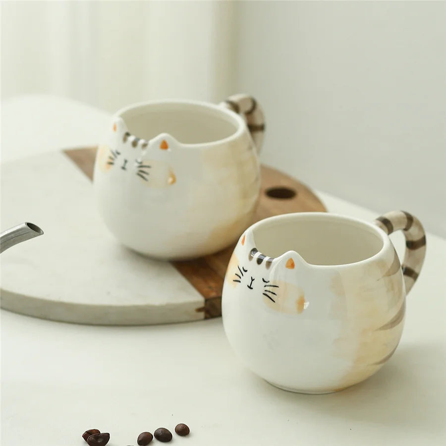 White ceramic cat mug with striped tail handle and painted whiskers face, coffee cup on wooden tray with teapot