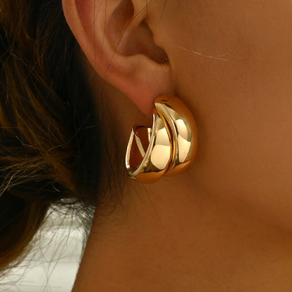Woman wearing large twisted gold-tone chunky hoop earrings with polished finish and layered crossover design