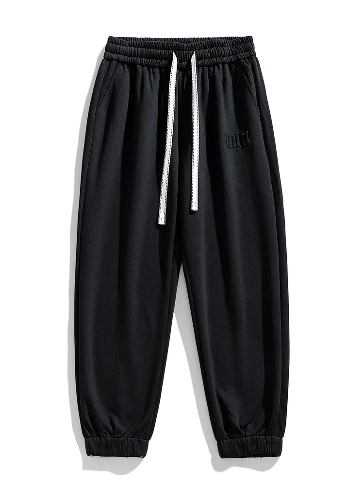 Black tapered knit joggers with elastic waistband, white drawstring, side pockets, and ribbed ankle cuffs