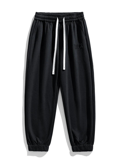 Black tapered knit joggers with elastic waistband, white drawstring, side pockets, and ribbed ankle cuffs