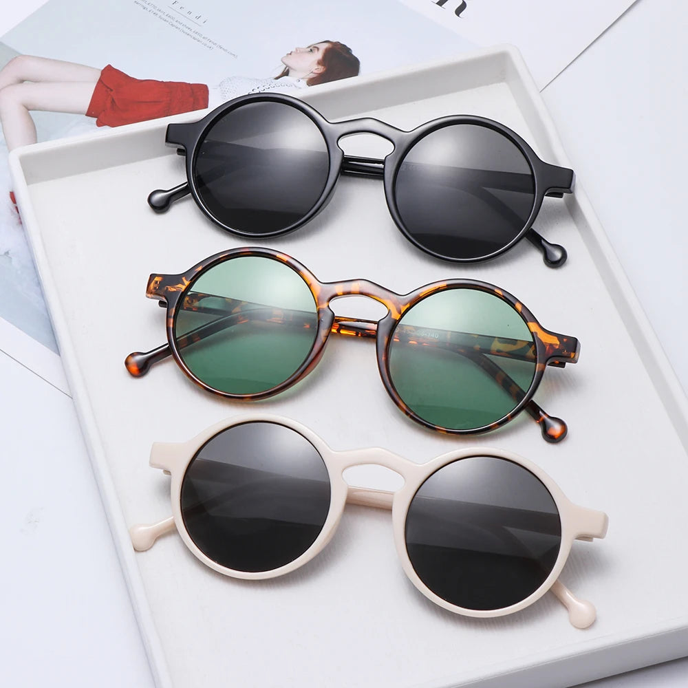 Three round frame sunglasses in black, tortoise with green lenses, and cream displayed on white tray with UV400 protection