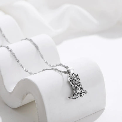 Silver necklace with intricate filigree western cowboy boot charm pendant on delicate chain, displayed on white prop