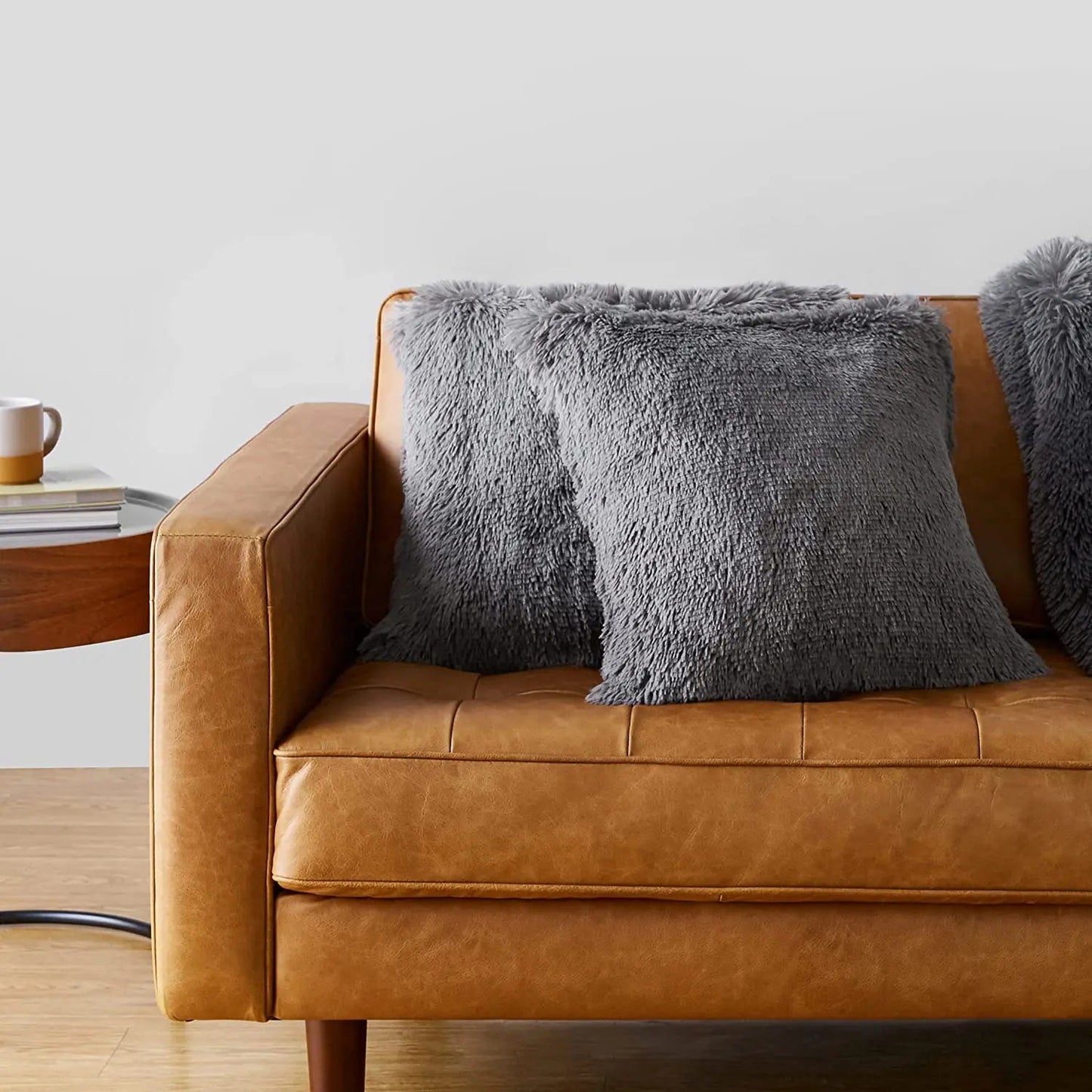 Gray faux fur plush throw pillows on a tan leather tufted sofa in a modern living room setting.