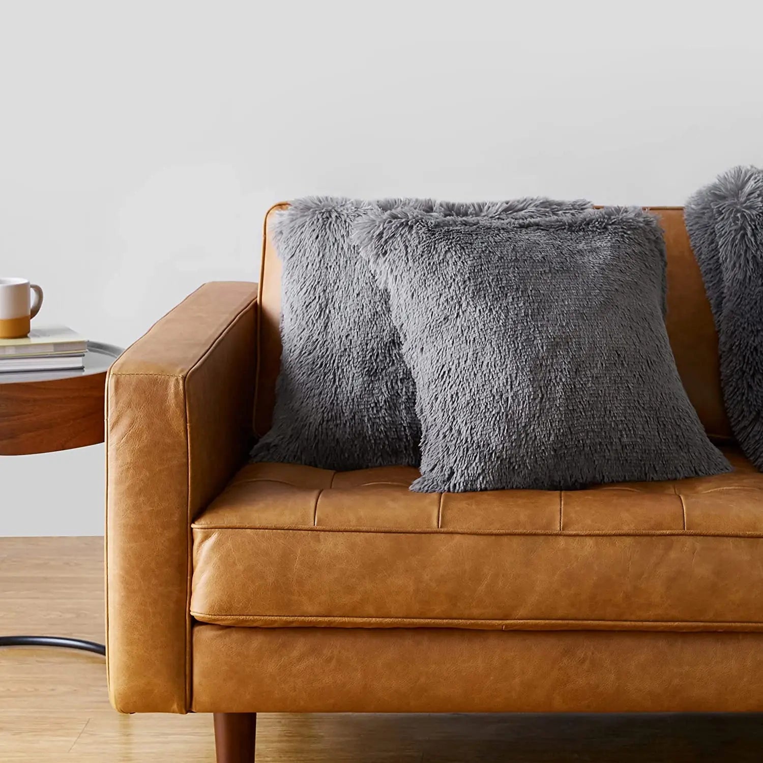 Gray faux fur plush throw pillows on a tan leather tufted sofa in a modern living room setting.