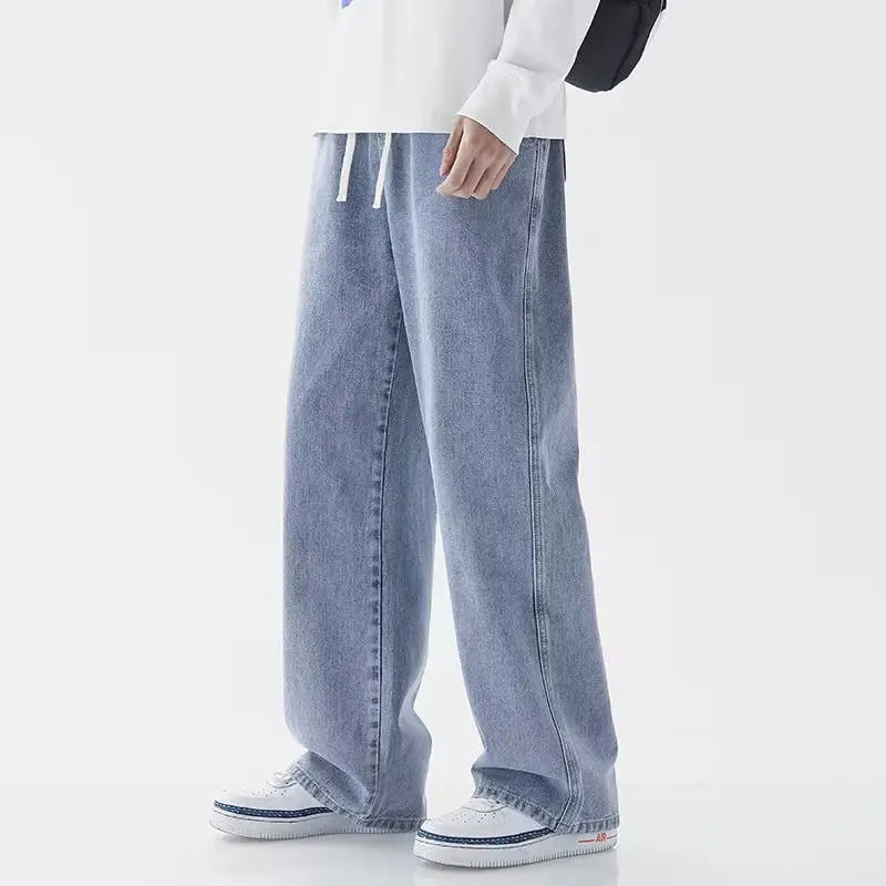 Man wearing light blue wide-leg relaxed fit denim jeans with drawstring waist, paired with white sneakers and sweatshirt