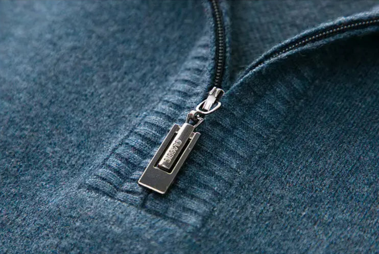Close-up of a teal wool blend men's quarter-zip sweater featuring a silver metal zipper pull with engraved branding.