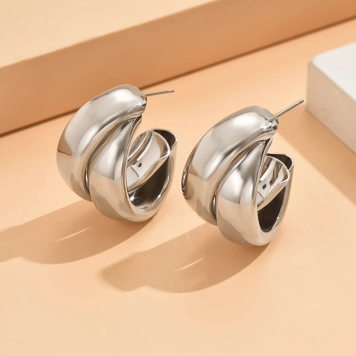 Silver twisted chunky hoop earrings with interlocking double-band design, shown as a pair on beige surface