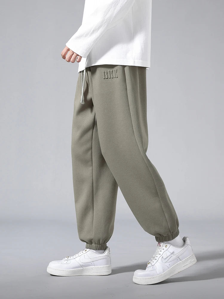 Men's olive green tapered knit joggers with elastic cuffs and drawstring waist, styled with white sneakers