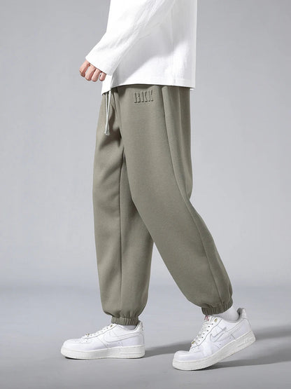 Men's olive green tapered knit joggers with elastic cuffs and drawstring waist, styled with white sneakers