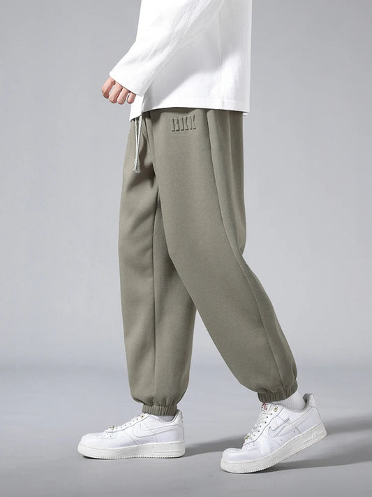 Men's olive green tapered knit joggers with elastic cuffs and drawstring waist, styled with white sneakers