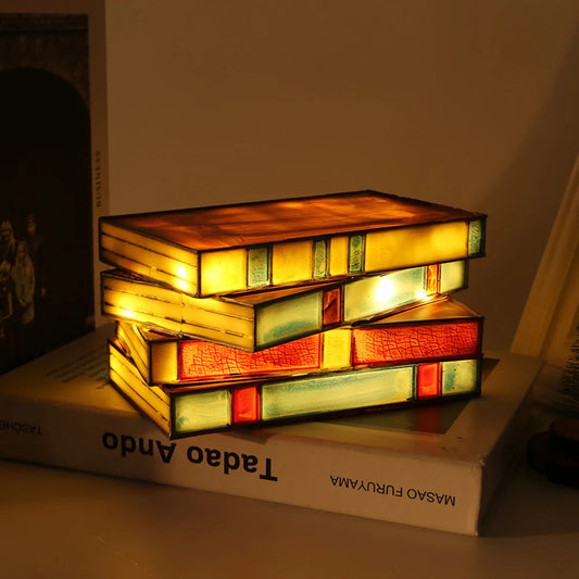 Stained glass stacked books night light lamp illuminated on desk with warm amber yellow red glow