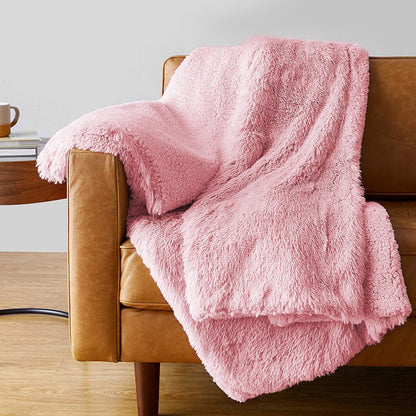 Pink fluffy faux fur plush throw blanket draped over a tan leather sofa with matching pillow