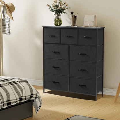 Black 9-drawer fabric dresser with steel frame, topped with flowers and accessories, placed beside a plaid-covered bed.