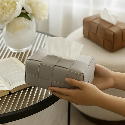 Hands holding a gray woven leather tissue box cover on a table, with a brown version visible in the background.