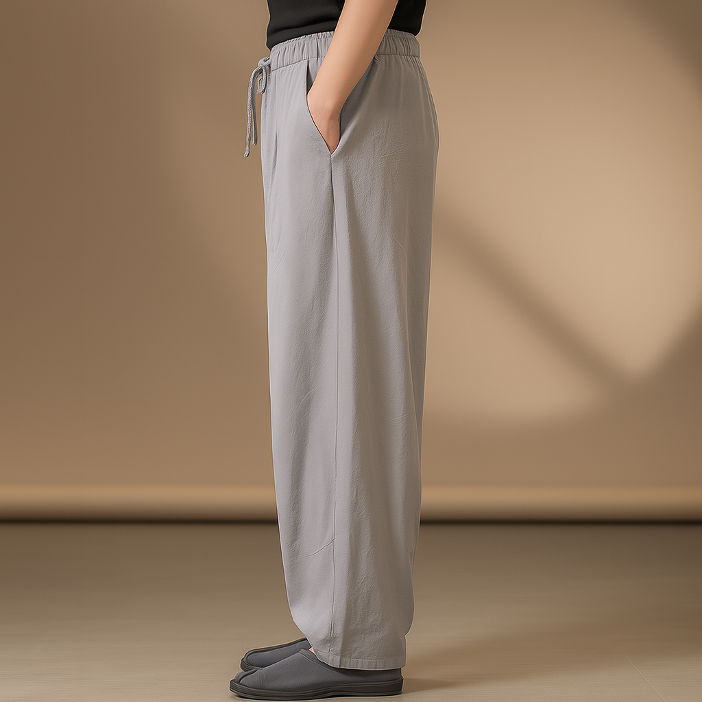 Men's light gray wide-leg linen drawstring pants with elastic waist and side pocket, worn with black slippers.