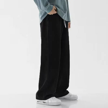 Man wearing black wide-leg relaxed fit denim jeans with drawstring waist, paired with white sneakers and teal top.
