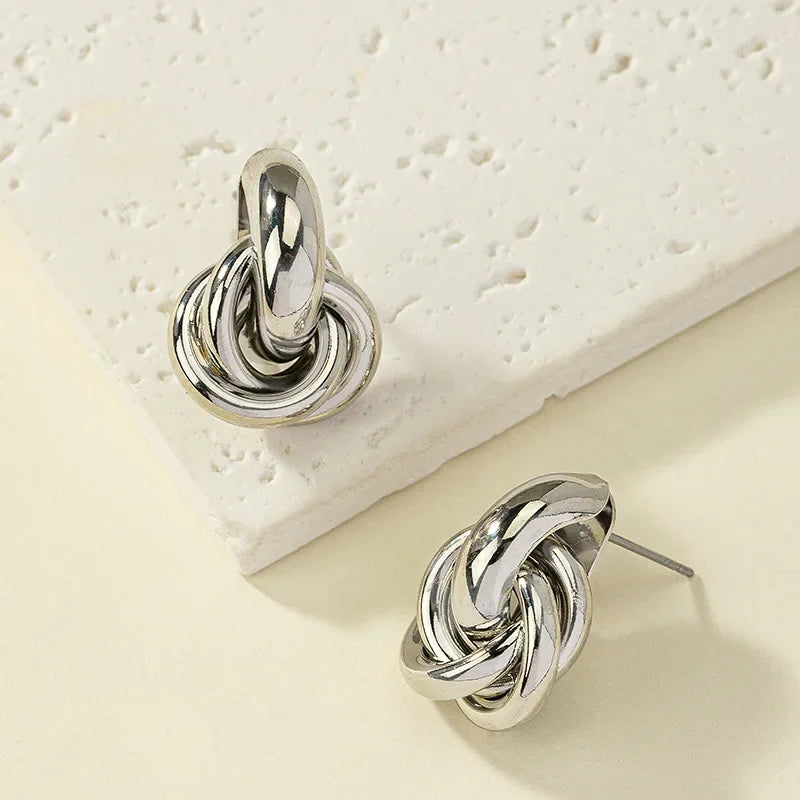 Silver interlocked knot stud earrings with twisted multi-ring design, shown on white textured surface