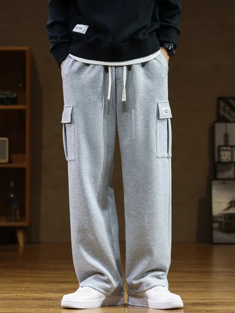 Gray men's relaxed fit cargo sweatpants with side pockets, drawstring waist, worn with black sweatshirt and white sneakers.
