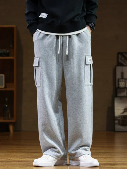 Gray men's relaxed fit cargo sweatpants with side pockets, drawstring waist, worn with black sweatshirt and white sneakers.