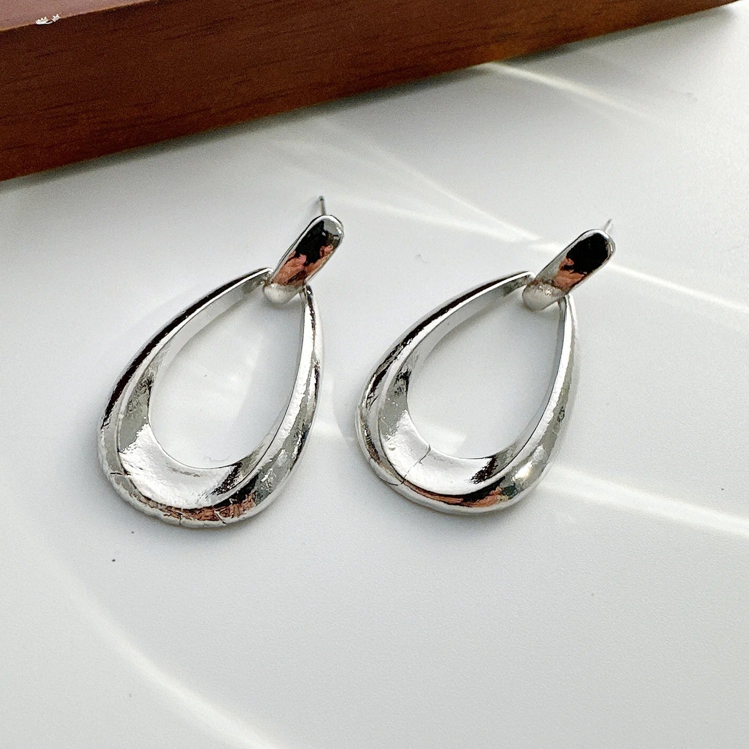Silver teardrop hoop drop earrings with polished finish and post backing, displayed on white surface