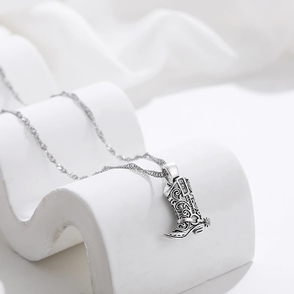 Silver necklace with intricate filigree cowboy boot charm pendant displayed on white ceramic jewelry stand