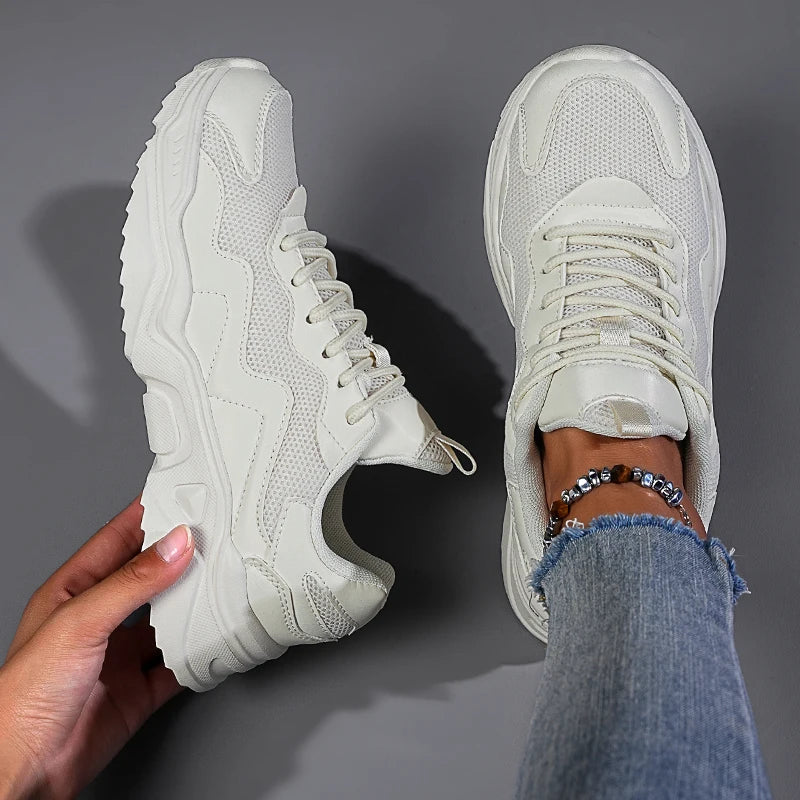 White mesh lace-up chunky sneakers shown from top view, one held by hand, one worn with distressed jeans and beaded anklet