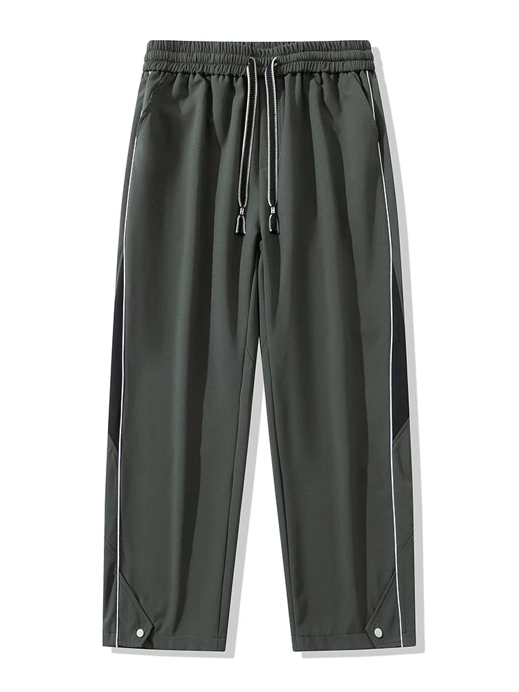 Men's wide-leg track pants in dark gray with black side panels, white piping, elastic drawstring waist, and snap hem details.