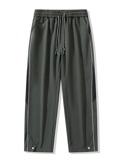 Men's wide-leg track pants in dark gray with black side panels, white piping, elastic drawstring waist, and snap hem details.