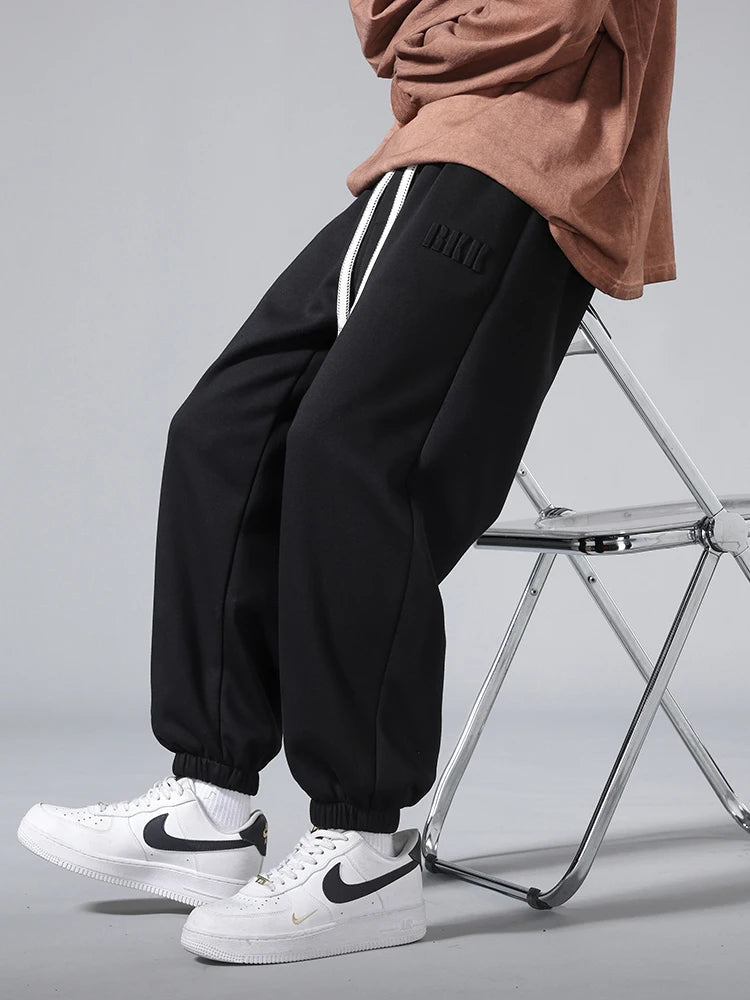 Men's black tapered knit joggers with white side stripes, elastic cuffs, paired with Nike Air Force 1 sneakers.